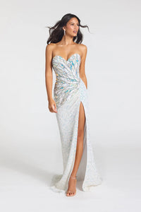 A woman modeling a strapless formal gown with a sweetheart neckline, ruched waist, high thigh slit, and a flowing train. The dress is heavily embellished with iridescent sequins that shift between silver, white, and light blue, set against a plain light gray studio background.
