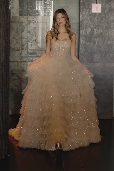 A captivating strapless sequin tulle ball gown with a sheer corset bodice, high slit, and ruffle skirt. Perfect for making a statement at prom night. Available at Madeline's Boutique in Toronto and Boca Raton.  Video of model wearing dress.