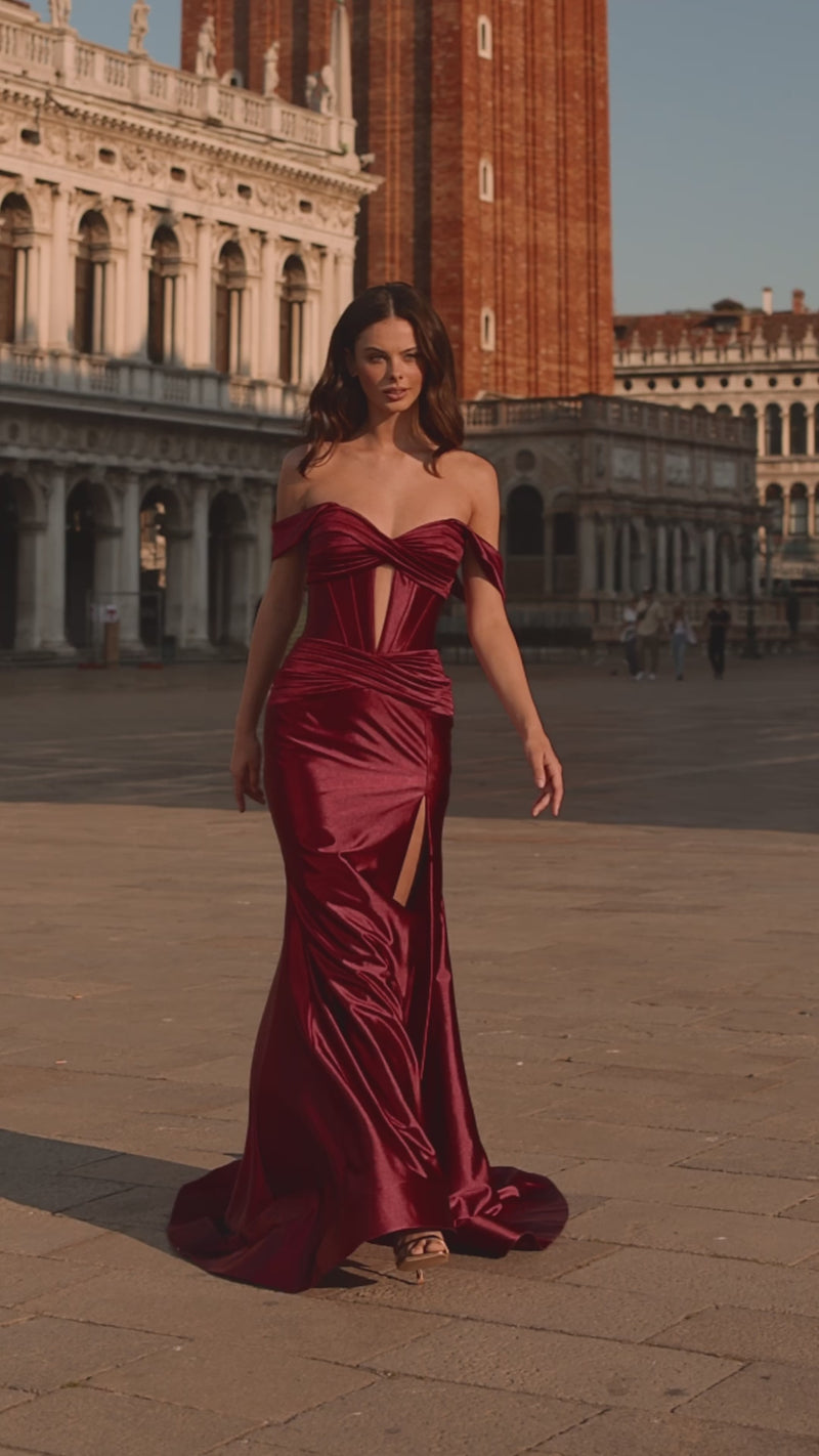 Model wearing Sherri Hill 57253 off-shoulder corset gown with lace-up back, ruched detailing, and high slit, styled for a red-carpet evening.