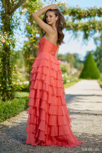 Woman in a coral ruffled gown standing outdoors with greenery in the background