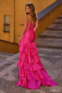 Woman in a pink ruffled gown standing on steps with a yellow wall in the background