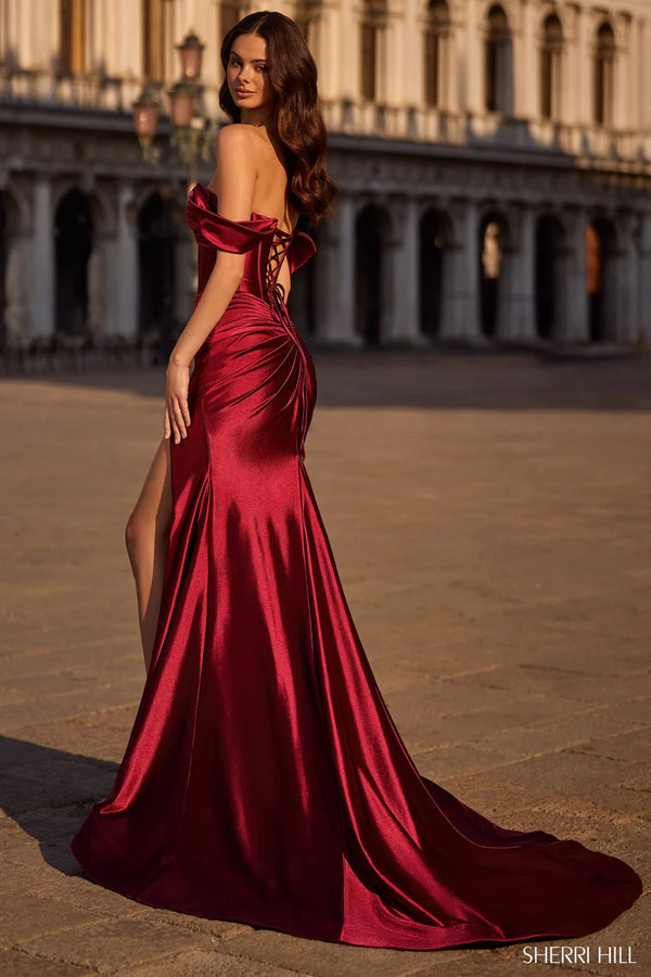 Woman in a burgundy evening gown with a high slit standing in an outdoor setting.