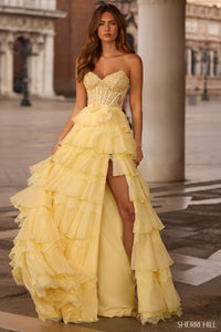 Woman wearing a yellow lace evening gown with a high slit in an outdoor setting.