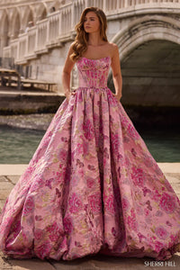 Woman in a pink floral gown standing by a bridge in an urban setting