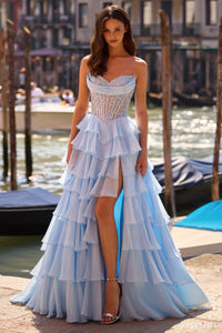 Model wearing Sherri Hill 57542 strapless lace corset ballgown with ruffled layered skirt and slit, posing by a waterfront.