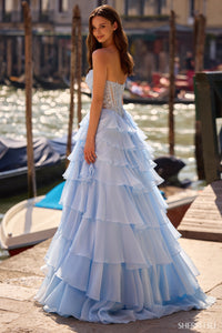 Model wearing Sherri Hill 57542 strapless lace corset ballgown with ruffled layered skirt and slit, posing by a waterfront.