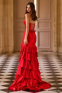 Woman wearing a red evening gown with ruffled layers in an elegant room.