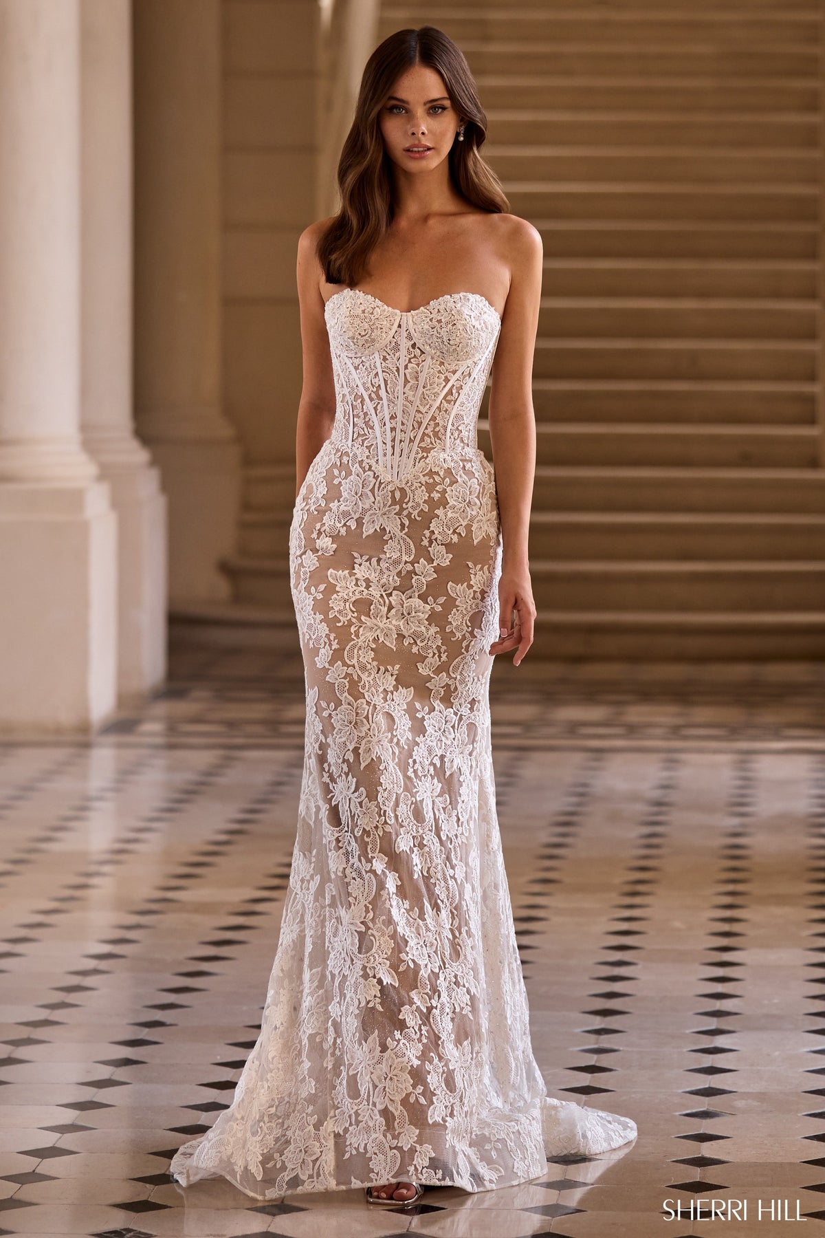 Woman wearing a strapless lace evening gown in an elegant indoor setting.