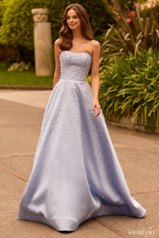 Model wearing Sherri Hill 58012 strapless ball gown with pearl embellishments, full skirt, side pockets, and lace-up back.