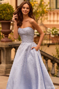 Model wearing Sherri Hill 58012 strapless ball gown with pearl embellishments, full skirt, side pockets, and lace-up back.