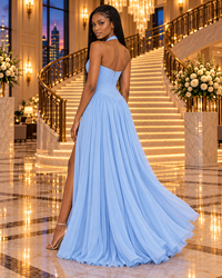 A woman wearing a light blue strapless A-line evening gown with a high thigh slit, standing in a grand hotel lobby with a staircase and warm chandeliers in the background.