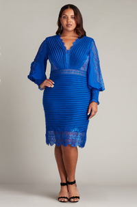 A woman wearing a knee-length pleated textured crepe cocktail dress with Bishop sleeves and a peekaboo lace hem, perfect for elegant evening occasions.