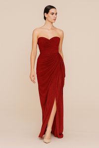 Woman wearing a strapless red gown with a slit on a beige background