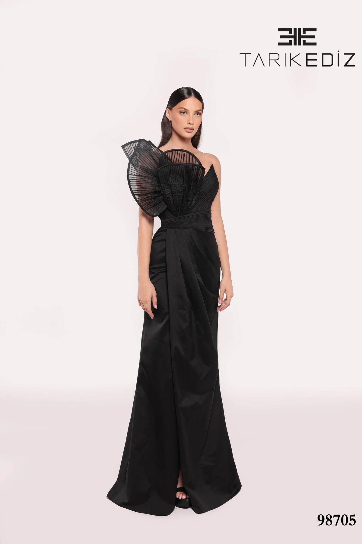 Woman wearing a black evening gown with sheer sleeves on a white background, featuring the brand 'TARIKE DIZ'.