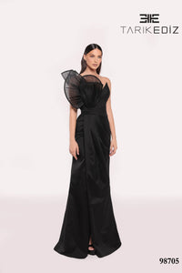 Woman wearing a black evening gown with sheer sleeves on a white background, featuring the brand 'TARIKE DIZ'.