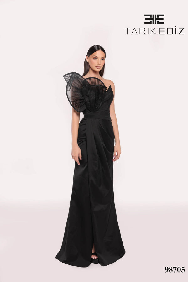 Woman wearing a black evening gown with sheer sleeves on a white background, featuring the brand 'TARIKE DIZ'.