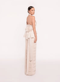 Model wearing the Tarik Ediz 98819 halter plunge neckline column gown with tiered skirt detailing, open back, floral accent, and long sash.