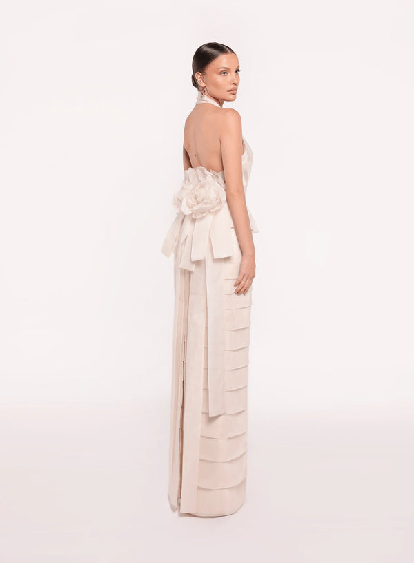 Model wearing the Tarik Ediz 98819 halter plunge neckline column gown with tiered skirt detailing, open back, floral accent, and long sash.