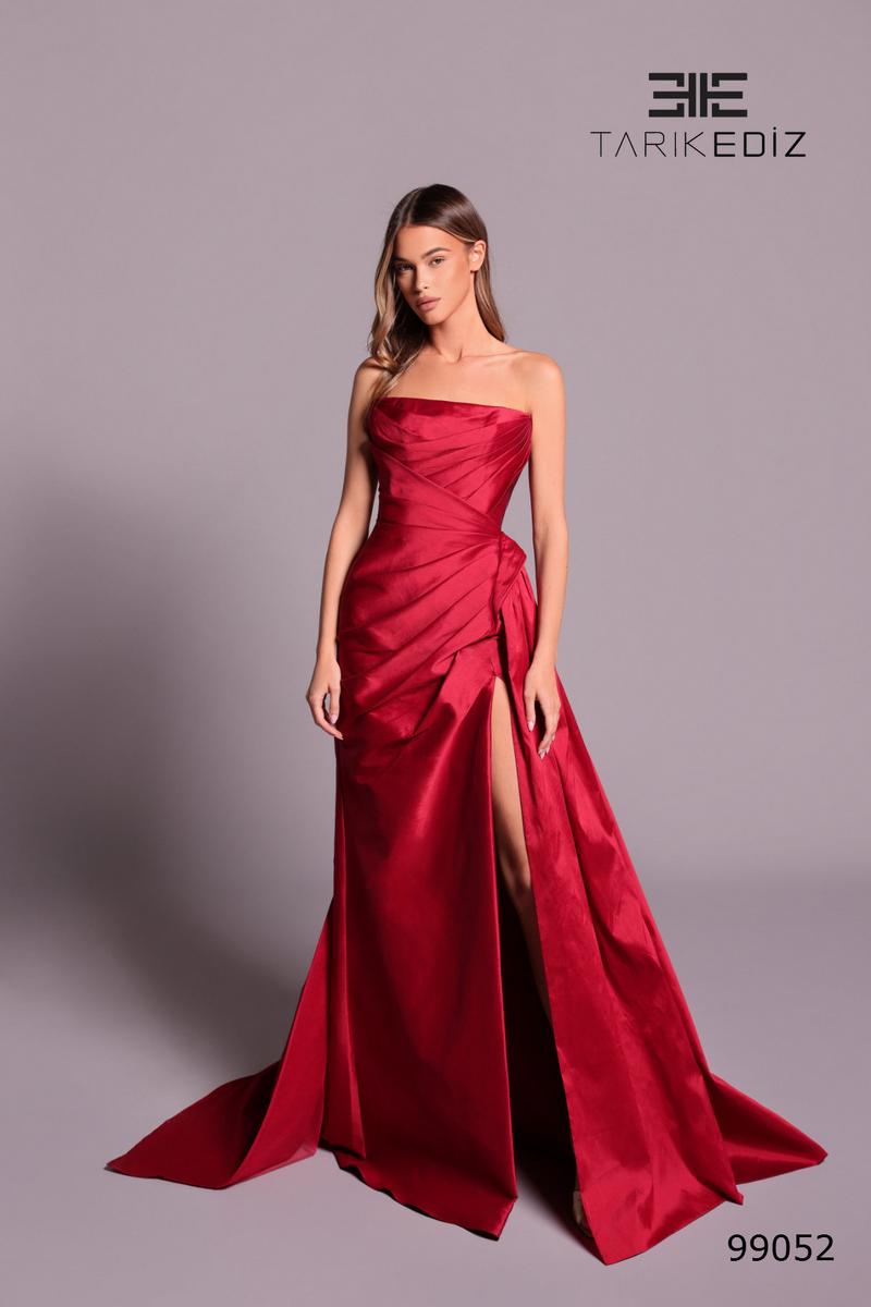 Red strapless gown with a slit on a gray background, featuring the brand 'Tarik Ediz'.