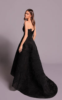 Woman wearing a black strapless gown with a long train on a plain background