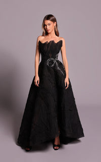 Woman wearing a black strapless gown with intricate detailing on a gray background