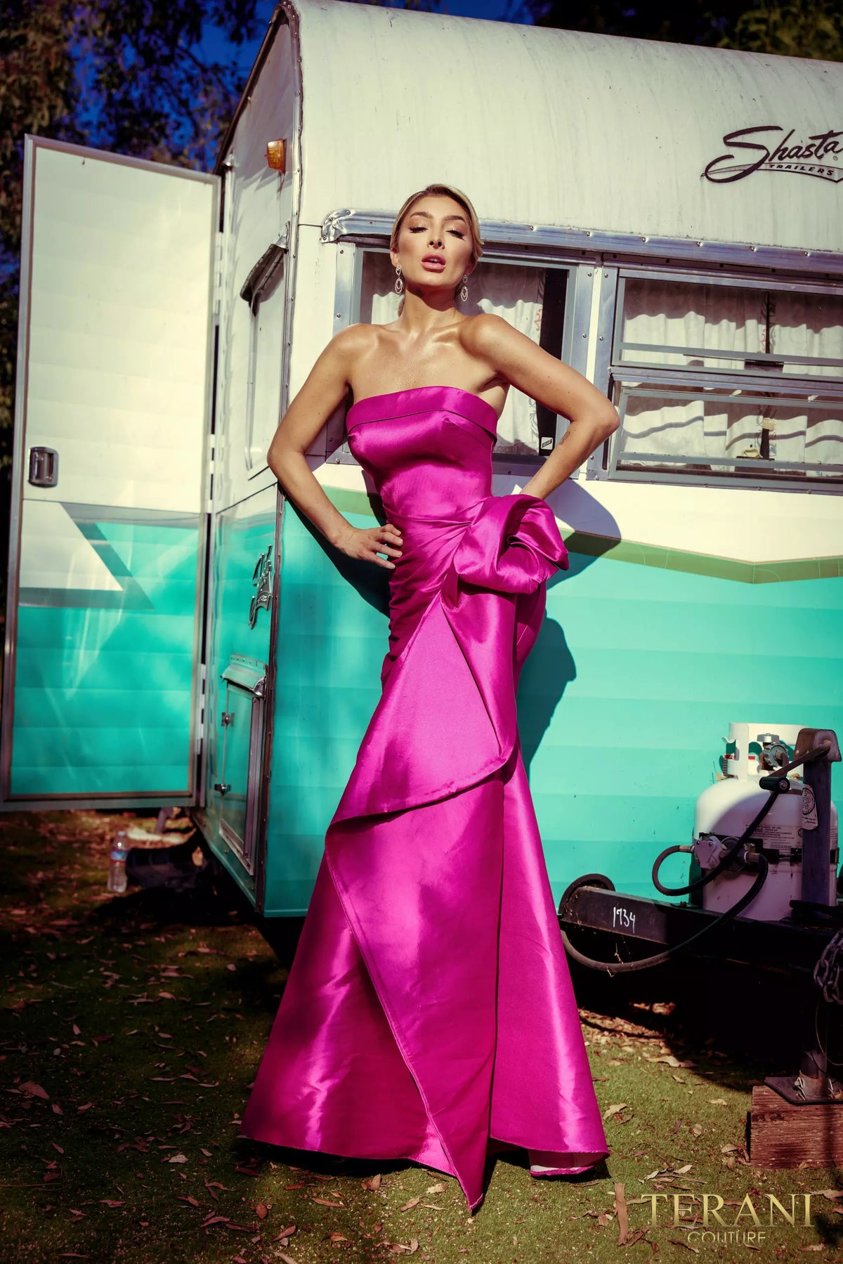 A stunning Mikado evening dress by Terani with an off-shoulder neckline, open back, and a draped bow feature on the waist. Perfect for evening events and as a mother-of-the-bride or mother-of-the-groom dress.  Color Fuschia in the picture.