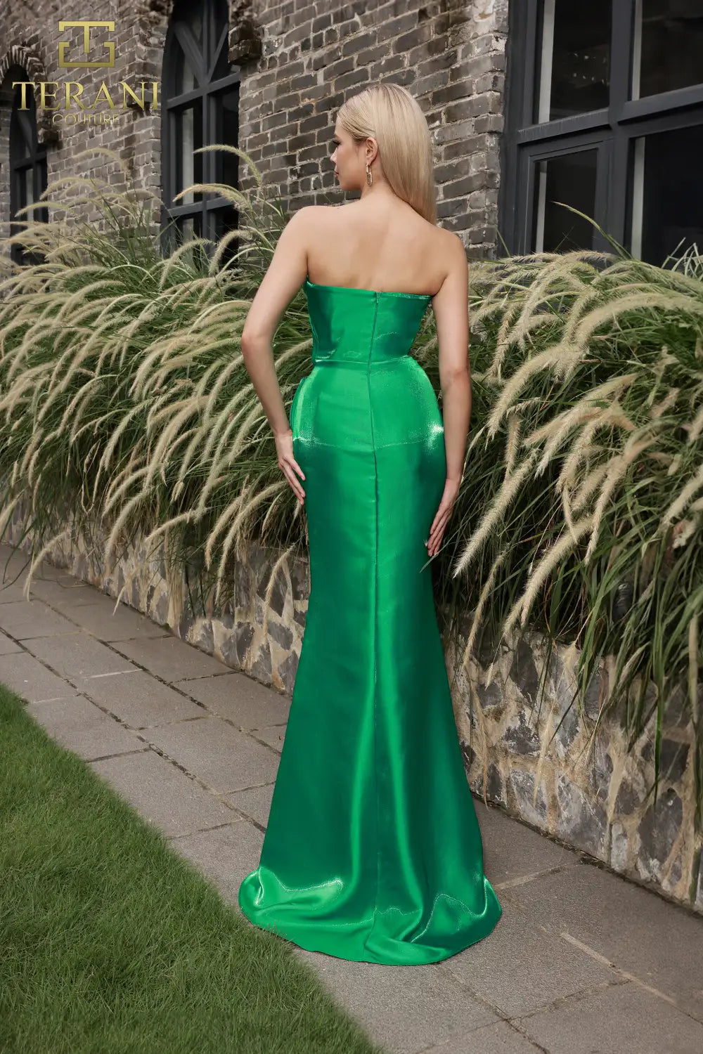 Model wearing Terani Couture 251E4231 one-shoulder gown with ruffle detail and floor-length silhouette.  In emerald.  Back View.