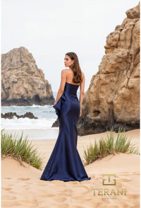 Model wearing Terani Couture 252E5550 strapless gown with peplum detail and mermaid silhouette on the beach.  Model is wearing the dress in the color Navy.  Back view of the dress.