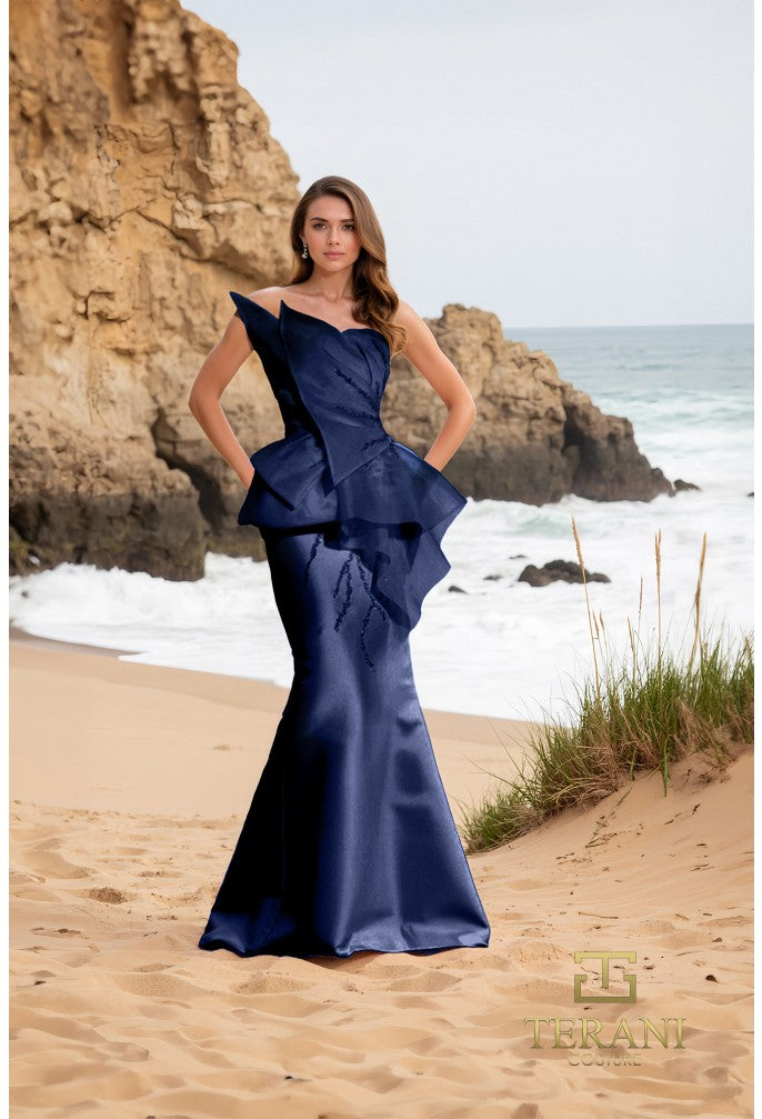 Model wearing Terani Couture 252E5550 strapless gown with peplum detail and mermaid silhouette on the beach.  Model is wearing the dress in the color Navy.