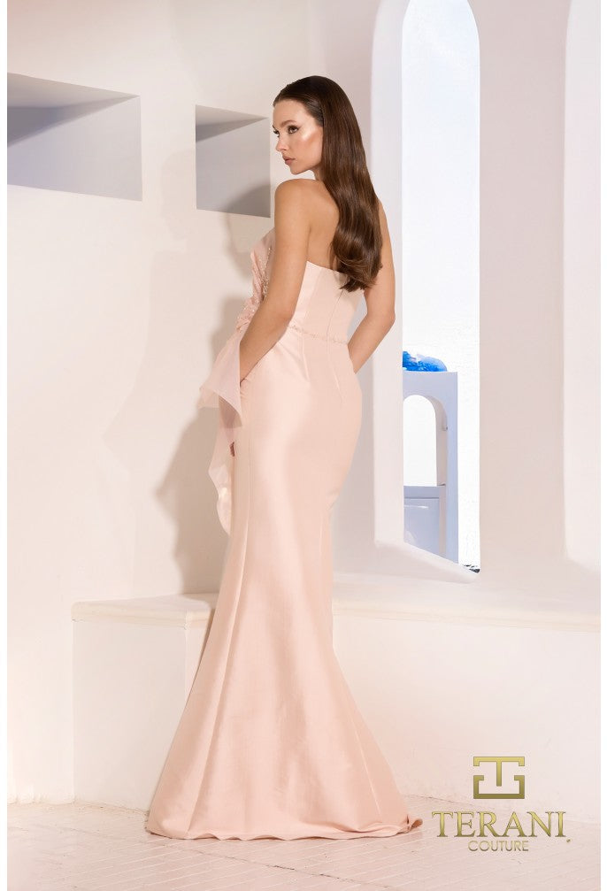Model wearing Terani Couture 252E5550 strapless gown with peplum detail and mermaid silhouette on the beach.  Model is wearing the dress in the color blush.  Back view.