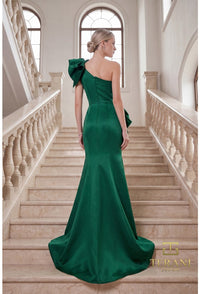 Model wearing Terani 262E7132 one-shoulder mermaid gown in the color emerald with draped bodice, statement bow accents, fitted silhouette, and sweep train.