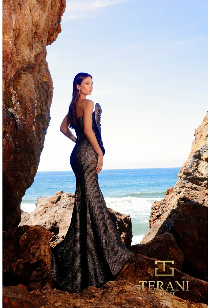 Woman in a elegant gown standing among rocks with ocean view, Terani brand visible