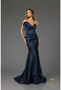 Woman wearing a blue evening gown with a textured pattern on a gray background, featuring the Terani brand.