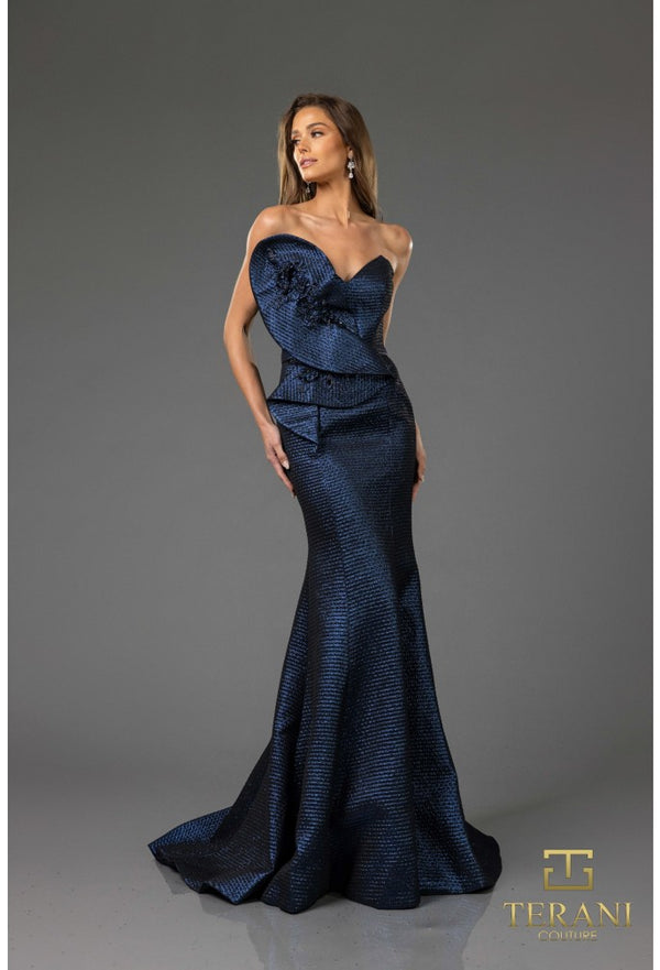 Woman wearing a blue evening gown with a textured pattern on a gray background, featuring the Terani brand.