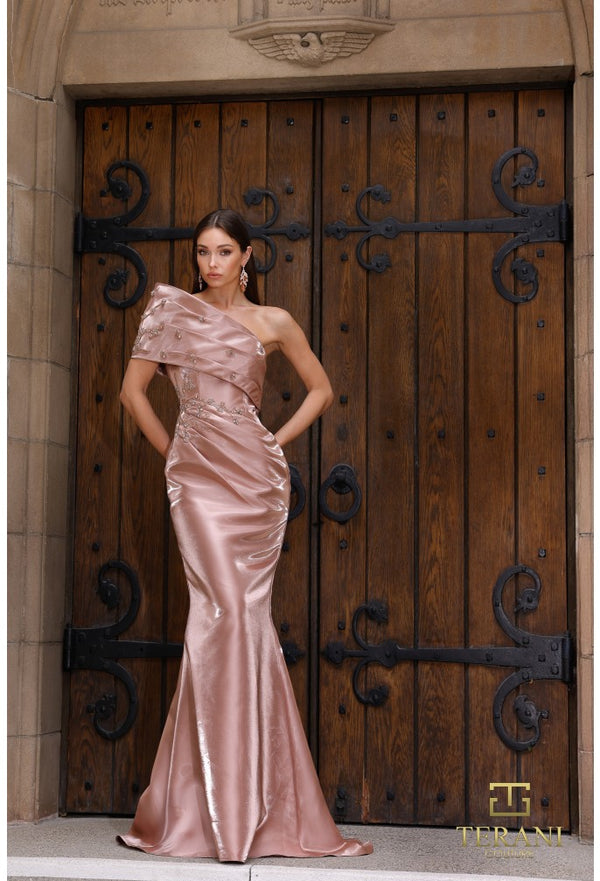 Woman in a pink evening gown standing in front of a large wooden door with metal handles.