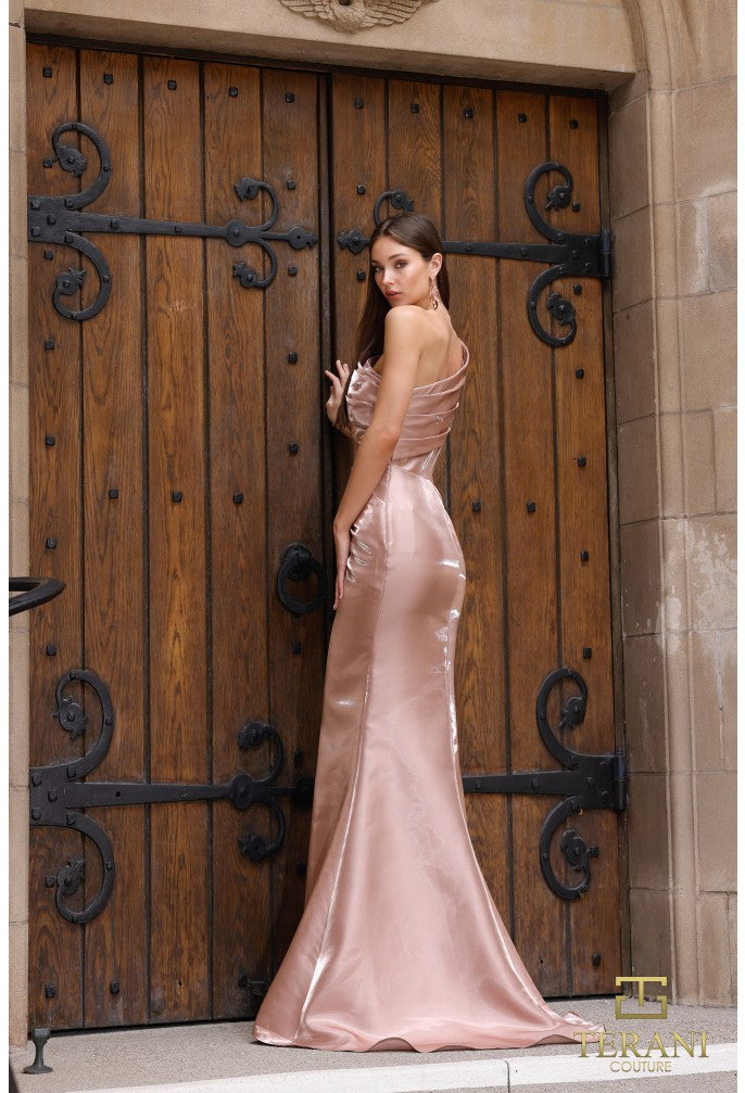 Woman in a pink evening gown standing in front of a large wooden door with intricate black metalwork.