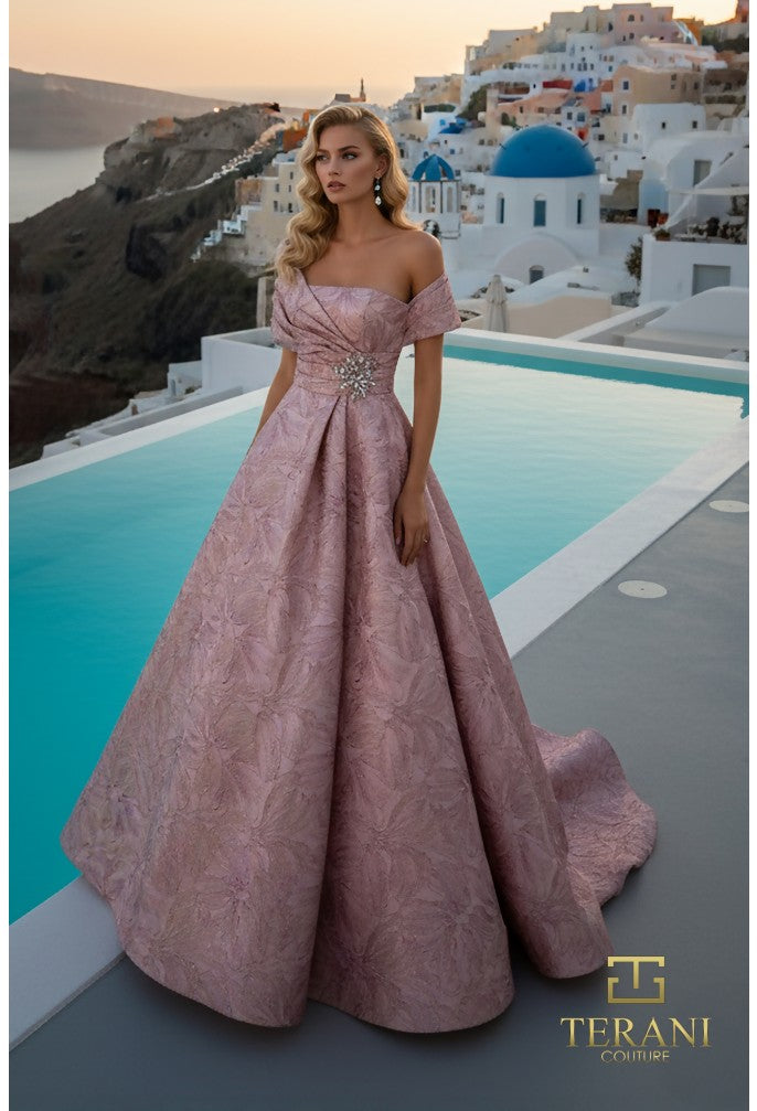 Woman in a pink gown standing by a pool with a scenic background, featuring Terani Couture logo.
