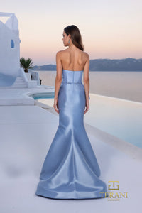 Woman in a light blue evening gown standing on a Mediterranean-style rooftop with a scenic view.