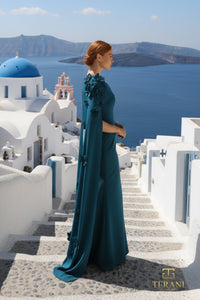Woman in a dark green dress standing on a staircase with a scenic view of the ocean and traditional buildings.