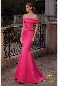 A woman models a fuchsia colored off-the-shoulder evening gown with floral embroidery on the bodice, standing on an outdoor stone terrace with a black wrought-iron railing. The Terani logo is visible in the bottom right corner.