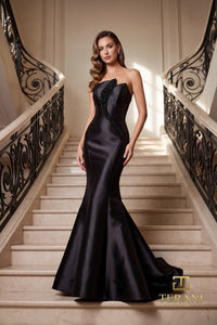 Woman in a black color Terani Couture evening gown standing on a balcony with classical architecture in the background.  Front View.