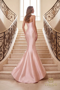 Woman in a blush color Terani Couture evening gown standing on a balcony with classical architecture in the background.