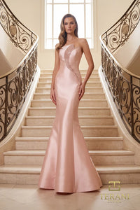 Woman in a blush color Terani Couture evening gown standing on a balcony with classical architecture in the background.