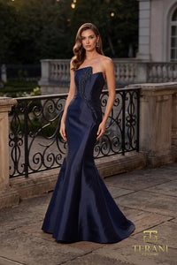Woman in a navy color Terani Couture evening gown standing on a balcony with classical architecture in the background.  Front View.