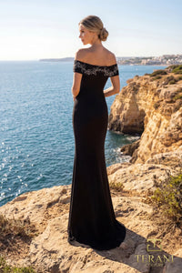Woman in a black gunmetal off-shoulder evening gown standing on a cliff overlooking the ocean.