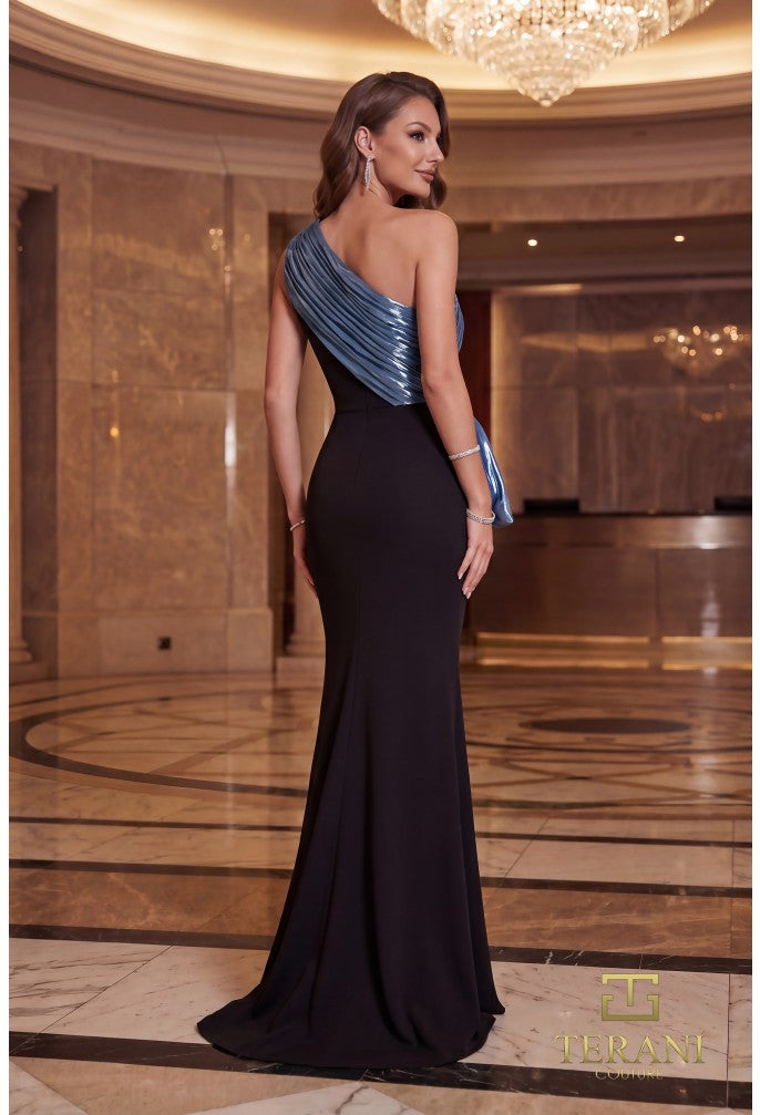 A woman models a floor-length evening gown in a grand hotel lobby. The dress features a black mermaid silhouette with a shimmering metallic blue one-shoulder draped bodice and matching blue sash at the waist.