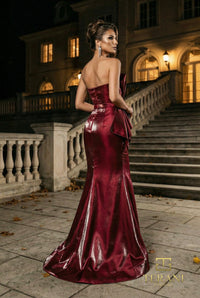 Woman in a wine color evening gown standing in front of an elegant building at night.