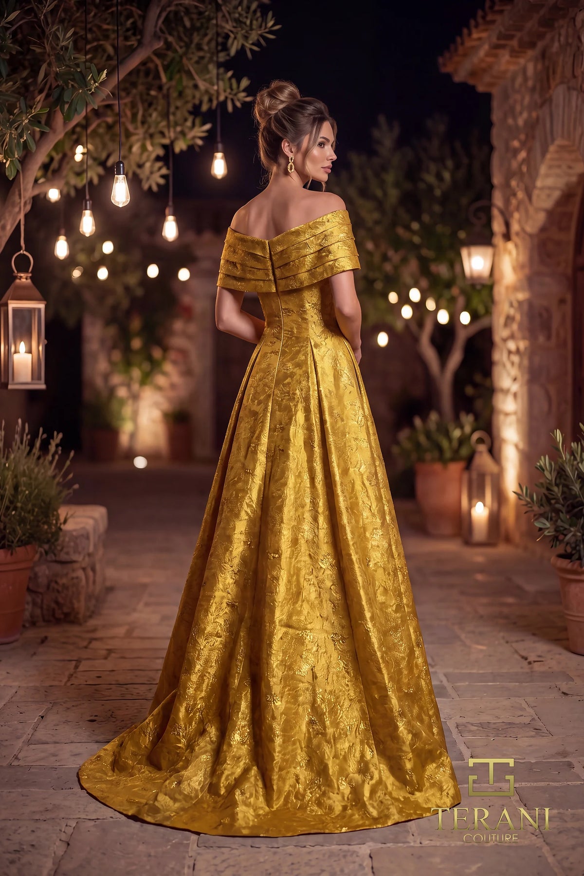 A woman stands in a courtyard at night wearing an off-the-shoulder floor-length gold gown with a textured jacquard pattern and a full skirt. Warm string lights and lanterns glow in the background.