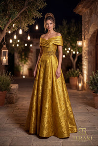 A woman stands outdoors at night wearing a voluminous off-the-shoulder gold ball gown with a textured jacquard pattern and a fitted bodice. The background features warm hanging lights, stone walls, and potted plants.