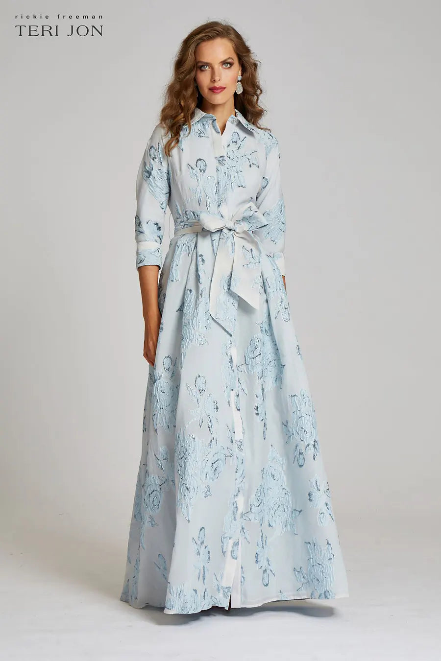 Model wearing Teri Jon 207015 floral shirt gown with a collared neckline, sash belt, three-quarter sleeves, and full A-line skirt.